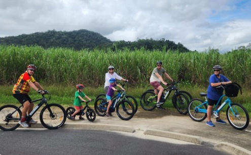 A family on bikes with a cane field in the back ground. 