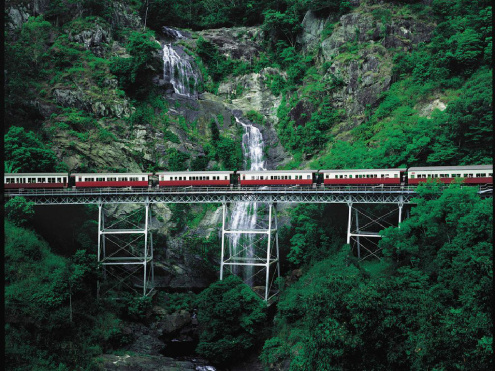 The Kuranda Scenic Railway on a bridge with a waterfall behind it. 