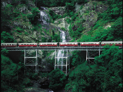The Kuranda Scenic Railway on a bridge with a waterfall behind it.