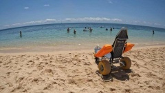 An image of a beach wheelchair on the sand at Green island, overlooking the water.