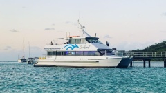 A commercial boat named 'QuickCoast' from Myroo Adventures docked by a pier in clear blue waters, with a sunset sky and other boats in the background