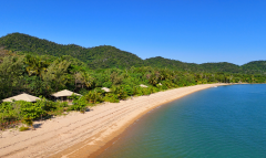 A remote beach with green hills in the background, small tents along the shoreline, and clear water.