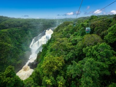 Aerial view of a cable car over a lush rainforest with a large waterfall in the background.
