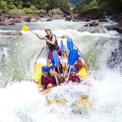 Six individuals wearing helmets and life jackets, navigating turbulent river waters in a raft.